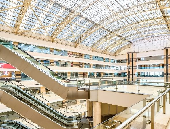 This is an inside shot of JMD Empire Square in Sector 28 Gurugram, taken from an upper floor balcony featuring a modern internal escalator system, polished floor passages, and a direct view of the wide glass roof structure.