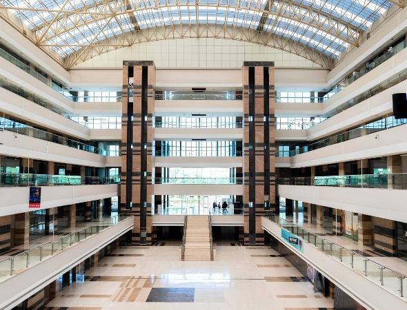 This is a symmetric interior shot inside JMD Empire Square in Sector 28 Gurugram, featuring the prominent twin elevator pillars, multi-level corporate glass corridors, and a spacious central ground floor courtyard.