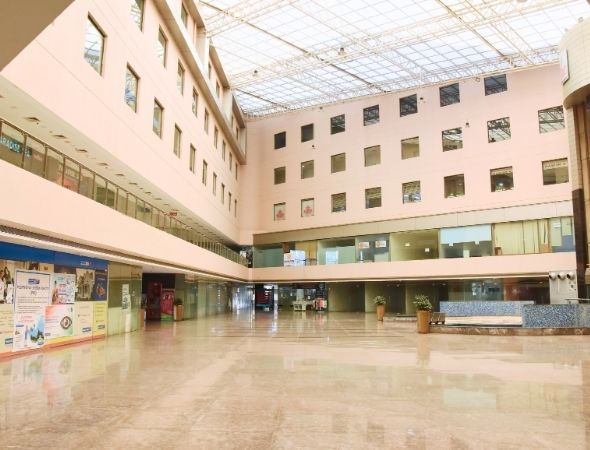 This is a JMD Galleria building in Sector 48 Gurugram showcasing an expansive wide-angle view of the polished marble ground floor plaza, highlighting the vast open commercial layout, multi-story office windows, and glass-front retail spaces stretching across the left wing.