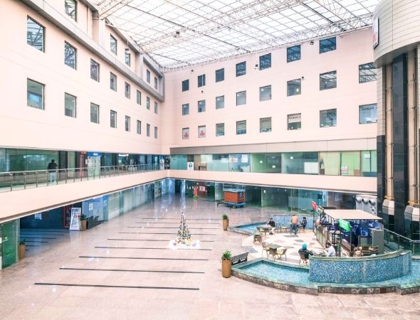 This is a JMD Galleria building in Sector 48 Gurugram showcasing a wide-angle inner shot of the expansive commercial complex corridors, featuring multi-tiered office balconies, polished flooring reflecting the skylight, and ground-floor glass retail showrooms.