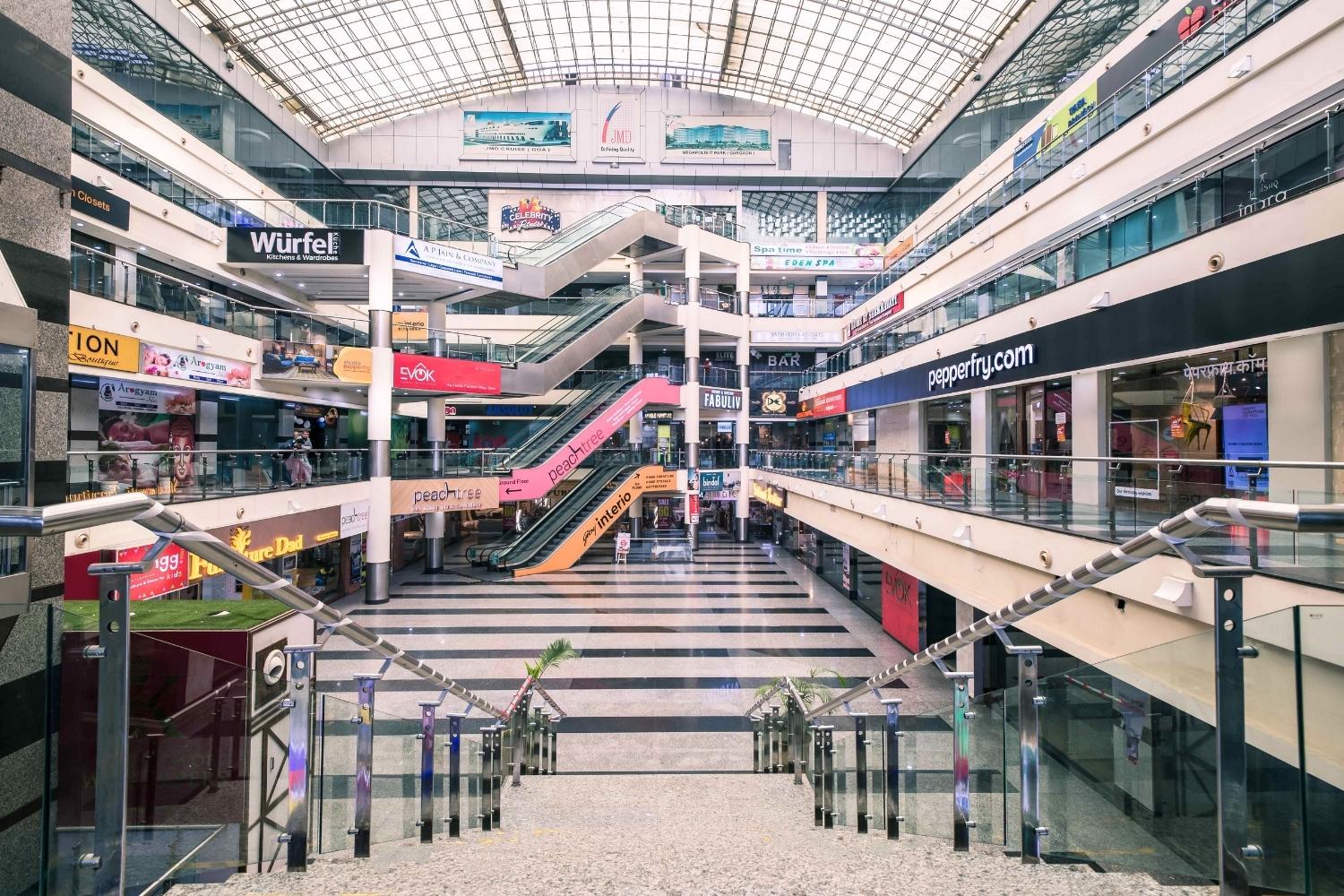This is the primary shopping atrium inside JMD Regent Arcade Gurugram, highlighting symmetric retail passageways, corporate presence, and open customer walkways within the mall.