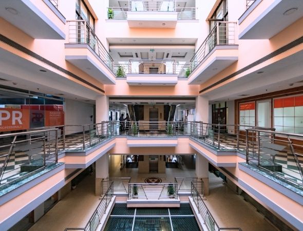 This is an inside shot of JMD Regent Plaza on MG Road Gurugram, highlighting the symmetric architectural design of its multi-story interior, featuring multiple levels of office balconies with steel handrails encircling the central courtyard.