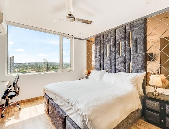 This is a JMD Suburbio 2 building in Sector 67 Gurugram showcasing a dual split view of a luxury studio apartment, featuring a bedroom with a plush king-size bed and tufted headboard