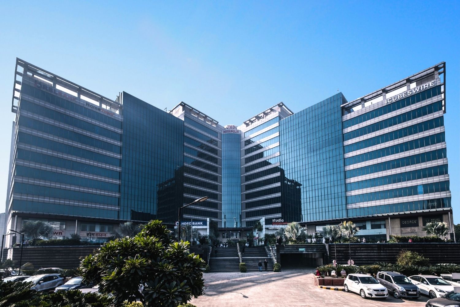 Wide-angle view of JMD Megapolis commercial tower building with its glass facade and a parking area in front.