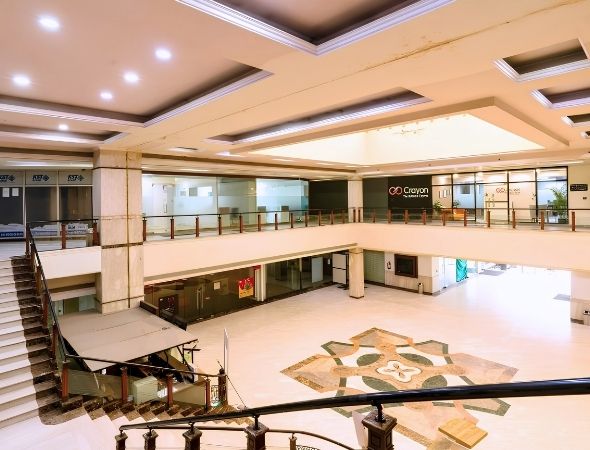 This is the central courtyard view inside JMD Regent Square on MG Road Gurugram, featuring dual retail escalators, a wide marble staircase leading to upper commercial floors, and a bright atrium layout with storefronts.